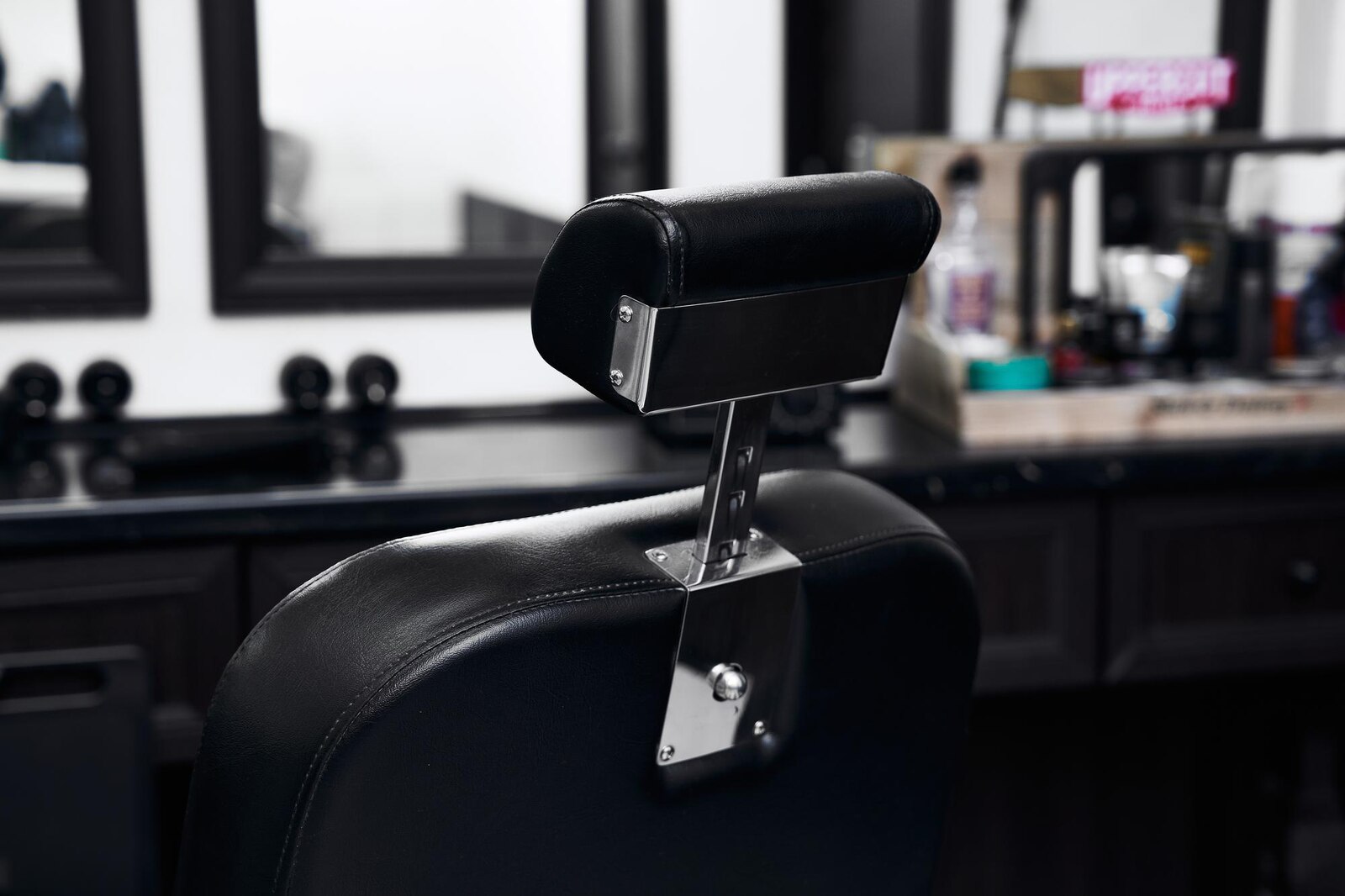 A black leather barber chair positioned in a contemporary salon with mirrors and tools visible.
