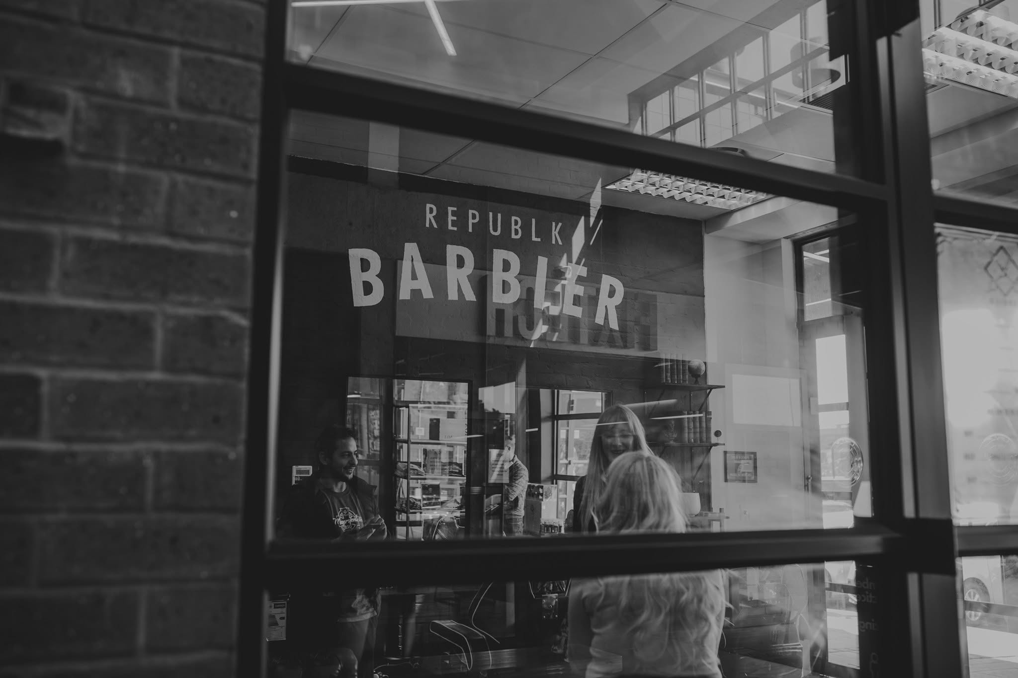 The shopfront of Barbier seen through its window, with the shop's name painted large on the wall inside and people talking beyond the glass.